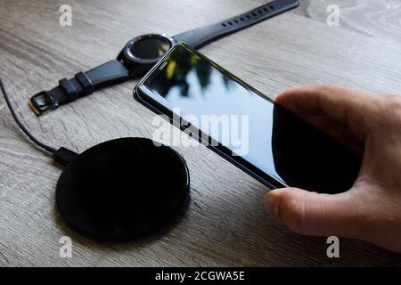 Le smartphone tenu dans la main est placé sur le chargeur sans fil. Montre intelligente en arrière-plan Banque D'Images