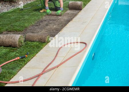 Travailleur en aménagement paysager installant des tourelles d'herbe de la nature de rouler à côté de la piscine extérieure résidentielle. Thème de l'industrie du jardinage et de l'aménagement paysager. Banque D'Images