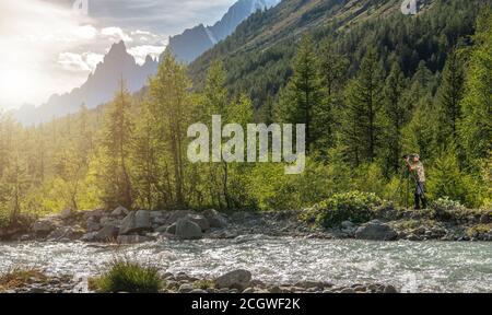 Photographe de la nature prendre des photos à l'aide d'un appareil photo professionnel à côté de Scenic Mountain River. Paysage alpin élevé en arrière-plan. Banque D'Images