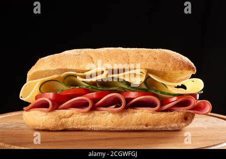 sandwich avec un pain ciabatta, fines tranches de saucisse et fromage edam sur bois brun, fond noir Banque D'Images