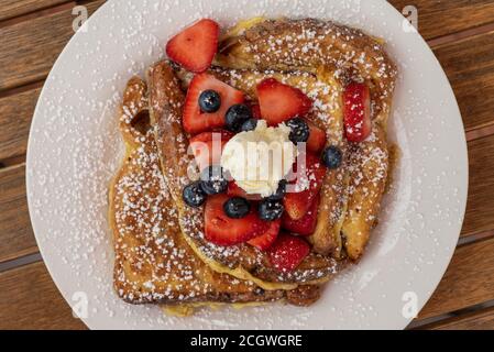 Toast français recouvert de bleu. Baies, fraises en tranches, sucre en poudre et beurre font un délicieux repas de petit déjeuner. Banque D'Images