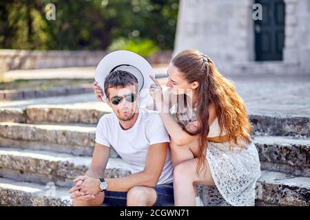 Couple amoureux assis sur des marches de pierre. Jeune femme portant un chapeau blanc sur la tête d'un homme en lunettes de soleil Banque D'Images