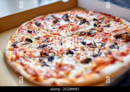 Pizza entière avec champignons, fromage et jambon dans une boîte en carton. Gros plan. Mise au point sélective Banque D'Images