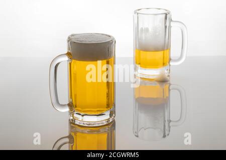 Tasses à bière avec bière. Bière sans glacer. Tasses à bière sur fond blanc rétroéclairé. Un verre presque vide et un plein. Banque D'Images