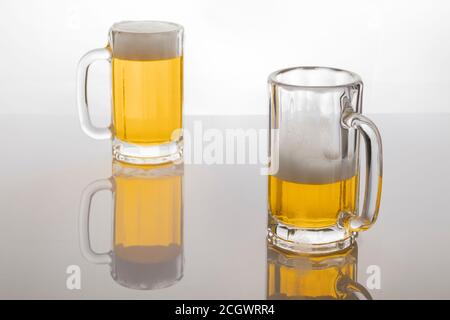 Tasses à bière avec bière. Bière sans glacer. Tasses à bière sur fond blanc rétroéclairé. Un verre presque vide et un plein. Banque D'Images