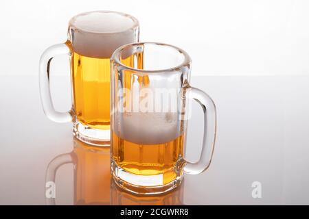 Tasses à bière avec bière. Bière sans glacer. Tasses à bière sur fond blanc rétroéclairé. Un verre presque vide et un plein. Banque D'Images