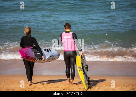 Homme et femme portant des combinaisons sur la plage avec leurs planches de surf, Sydney, Australie Banque D'Images