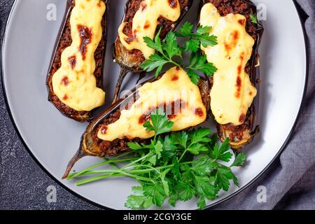 Plat grec de Papoutsakia : aubergines farcies cuites au four avec viande de bœuf, tomates, nappées de sauce au béchamel avec fromage, servies sur une assiette sur béton foncé Banque D'Images