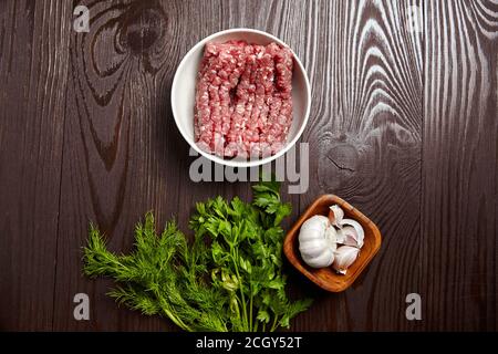 Bol avec bœuf haché cru et condiments sur table en bois, vue de dessus. Cuisson de viande hachée avec des assaisonnements frais, plat. Gousses et têtes d'ail blanches Banque D'Images