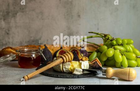 Camembert au four, branche de raisins verts, figues, miel, cassis, vin. Banque D'Images