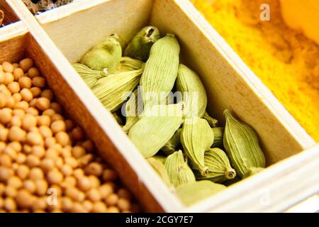 Cardamome vert ou graines de cardamon. Différentes épices sèches dans une boîte en bois. Moutarde et curcuma jaune sur fond Banque D'Images