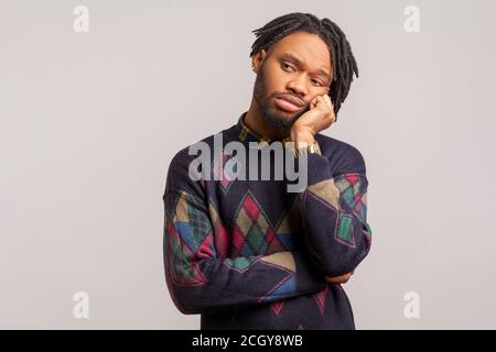 Homme africain endormi et fatigué avec des dreadlocks dans un sweat-shirt tendance pendu tête à la main avec un visage ennuyeux, déception, procrastination. Salle de studio intérieure Banque D'Images