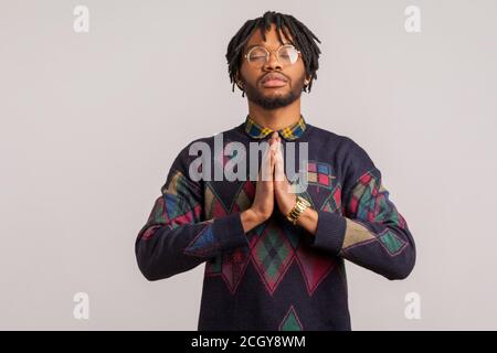 Gros plan l'homme africain concentré dans des lunettes avec des dreadlocks fermer les yeux et les mains pressantes ensemble essayant de se calmer, la pratique du yoga, le zen. Intérieur s Banque D'Images