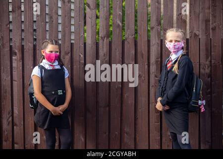 Deux écolières de 10 ans portant les uniformes et le visage de l'école masques et debout à côté d'une clôture en bois Banque D'Images