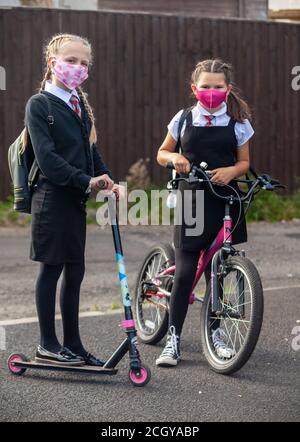 Deux écolières en uniforme scolaire debout avec leur vélo et leur scooter et portant des masques faciaux. Banque D'Images