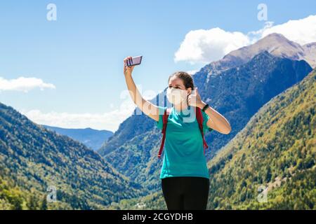 Photo d'une fille de randonneur prenant un selfie avec masque tout en appréciant une journée dans les montagnes et un beau paysage en arrière-plan Banque D'Images