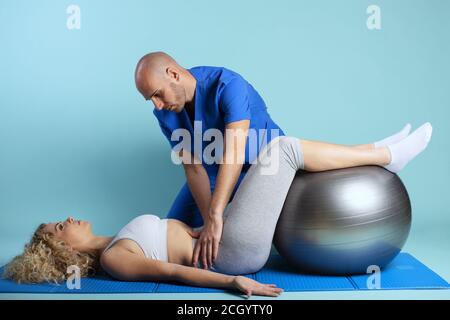 Fille effectue des exercices avec un physiothérapeute. Fond cyan Banque D'Images