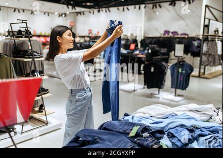 Une femme gaie qui choisit un Jean dans un magasin de vêtements Banque D'Images