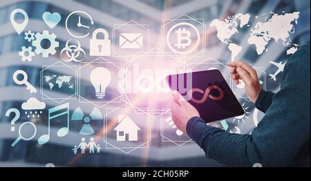 Personne utilisant une tablette pour afficher plusieurs icônes sous forme d'applications et de widgets multimédia, symbole infini au centre. Concept de développement technologique moderne, li Banque D'Images