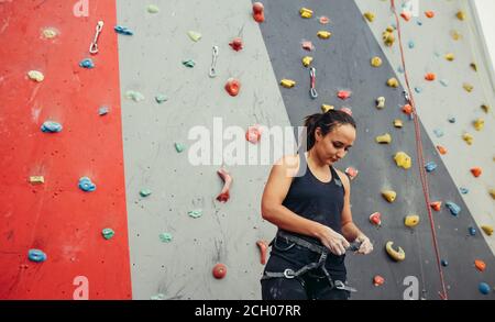 Athlète Forte femme met sur l'assurage faisceau pour la pratique sur un mur de pierre artificielle. Banque D'Images