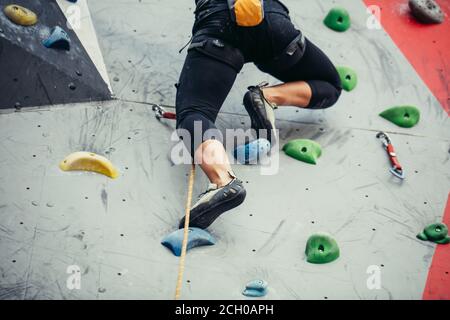 Leggs of sportswoman Rock Climber. Grimpeur de roche se déplaçant sur un mur artificiel rocheux. Jambes et chaussures d'escalade en gros plan. Banque D'Images