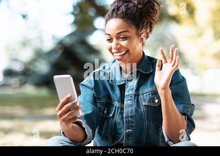 Femme noire avec un téléphone intelligent effectuant un appel vidéo en position de stationnement Banque D'Images