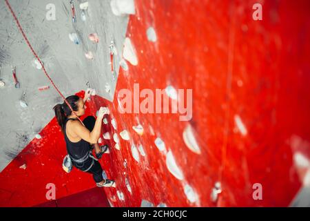 Portrait de femme aux cheveux brun sportif l'exercice de l'escalade sur rocher artificiel rouge coloré dans la salle d'escalade. Banque D'Images