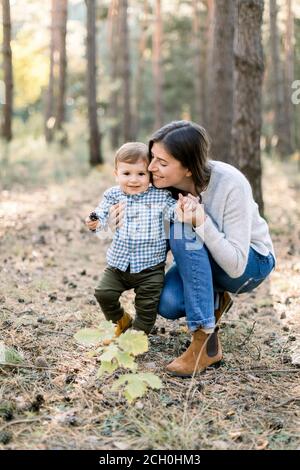 Jeune famille, femme heureuse maman s'amusant dans la forêt de pins d'automne avec son enfant petit fils. Mère embrassant son fils enfant lors de sa promenade dans le parc Banque D'Images