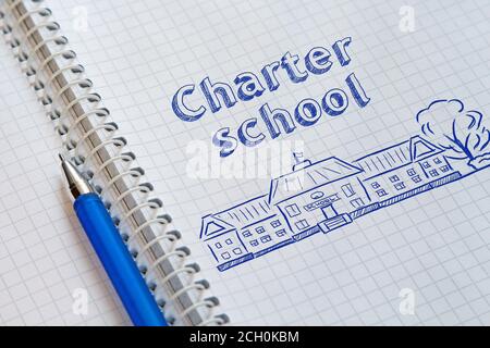 Ordinateur portable avec une spirale dans une cage et un stylo bleu dessus. Sur la page de gauche dessiné l'école et lettering Charter School Banque D'Images