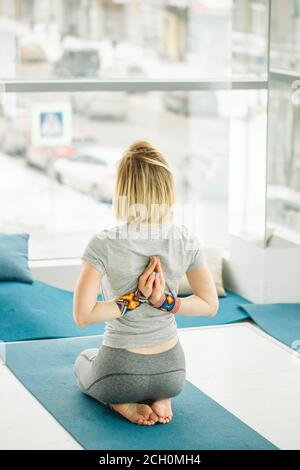 Jeune femme faisant un exercice de yoga sur le tapis dans Virasana ou Hero pose avec la prière inversée ou namaste en studio sur un arrière-plan marbré de l'arrière-plan. Banque D'Images