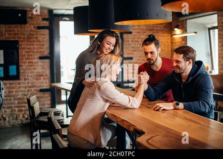 Jeunes femmes attirantes filles amies et leurs nouvelles amies masculines jouant, luttant et souriant tout en passant du temps ensemble au pub branché. Plaisir, vacances Banque D'Images