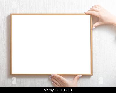 de belles mains pour femmes accrochent un cadre modèle au mur. Cadre de maquette. Banque D'Images