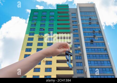 Clés dans la main d'une femme sur le fond d'un immeuble résidentiel de grande hauteur et ciel bleu. Concept immobilier. Banque D'Images