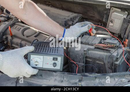 Gros plan des mains mâles vérifiant avec précision la tension de la batterie d'automobile sous le capot de la machine. Concept de contrôle automobile. Style de vie. Banque D'Images