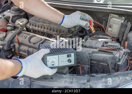 Un gros plan des mains d'un mécanicien utilisant des câbles volants sur une batterie de voiture. Concept de contrôle automobile Banque D'Images