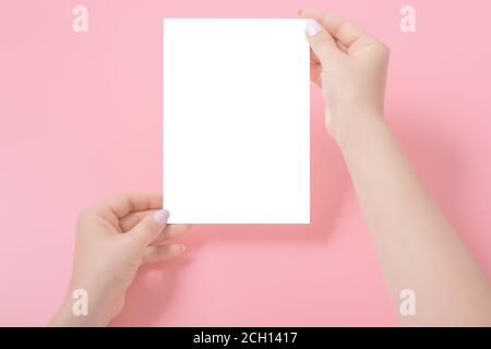 Mains de femme manucure tenant une carte postale sur fond rose. Modèle de maquette de carte ordinaire ou de feuille de papier vide. Banque D'Images