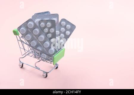 Grocery cart with pills, pharmacy shopping concept. Pills in the little grocery cart on pink background Stock Photo