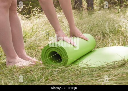 Femme roulant son tapis après un cours de yoga sur un pré vert un jour ensoleillé d'été. Concept de yoga dans la nature Banque D'Images