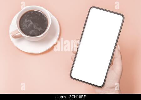 Mockup téléphone portable, smartphone. Les mains des femmes tiennent un téléphone portable avec un écran vierge sur fond rose. Une tasse de café sur la table rose. À Banque D'Images
