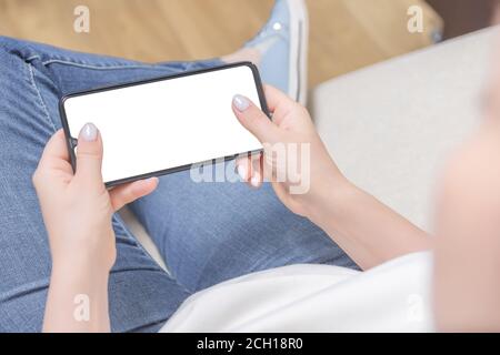 Mockup image of woman's hands holding white mobile phone with blank screen in horizontal position in horizontal position. Mockup cell phone. Top view. Banque D'Images