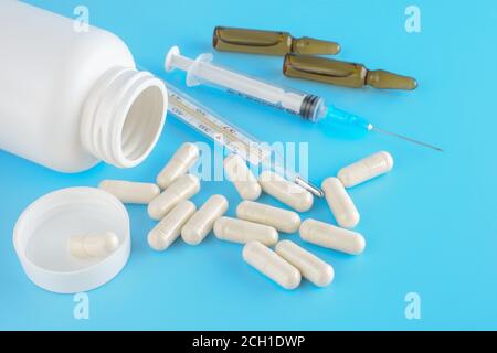 Des pilules débordent du contenant blanc. Récipients médicaux, pilules, seringues, ampoules pour injections sur fond médical bleu. Gros plan, vue de dessus. Banque D'Images