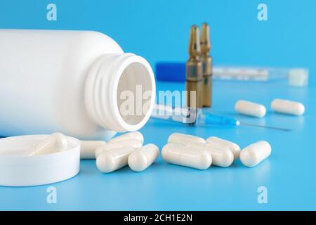 Des pilules débordent du contenant blanc. Récipients médicaux, pilules, seringues, ampoules pour injections sur fond médical bleu. Différents médicaments Banque D'Images