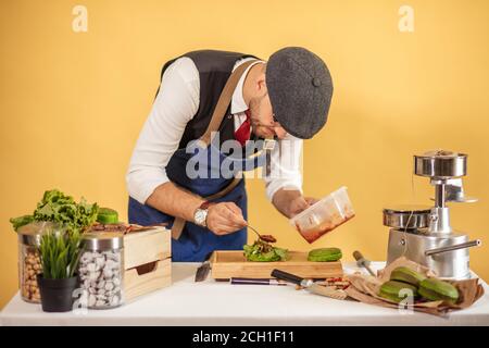 Processus de la cuisson des hamburgers en studio sur fond jaune. Maître gai composant le chef d'œuvre culinaire sur table. Concept cuisine Hamburger Banque D'Images