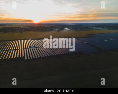 Vue aérienne de drone dans de grands panneaux solaires dans une ferme solaire dans un grand champ sur la campagne au coucher du soleil clair. Centrales solaires, photo colorée Banque D'Images