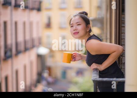 Jeune femme coréenne asiatique, belle et heureuse, jouissant d'une vue sur la ville Depuis le balcon de la chambre d'hôtel en Espagne pendant le voyage de vacances à Europe buvant du café relaxe Banque D'Images