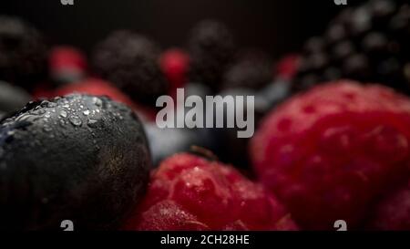 Vue rapprochée des baies fraîches. Framboises, mûres et bleuets sur fond noir. Savoureux fruits biologiques à l'aspect couvert de rosée. Banque D'Images