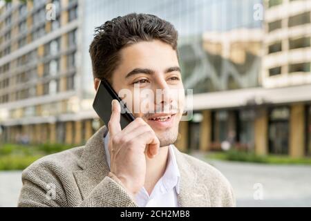 Joyeux jeune homme d'affaires de course mixte en tenue de formalwear parlant à des clients sur le téléphone Banque D'Images