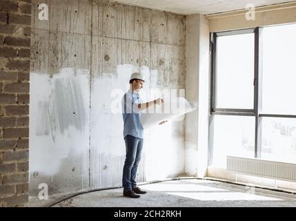 beau architecte doué tenant un plan de bâtiment dans la chambre avec entretien. vue latérale photo. Banque D'Images