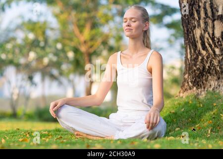 Jeune femme détendue méditant à la paix à l'extérieur assis au parc pendant l'été. Bien-être, santé et autosoins. Banque D'Images