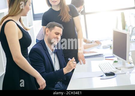 Joyeux leader caucasien assis est entouré de belles femmes à travailler au bureau Banque D'Images